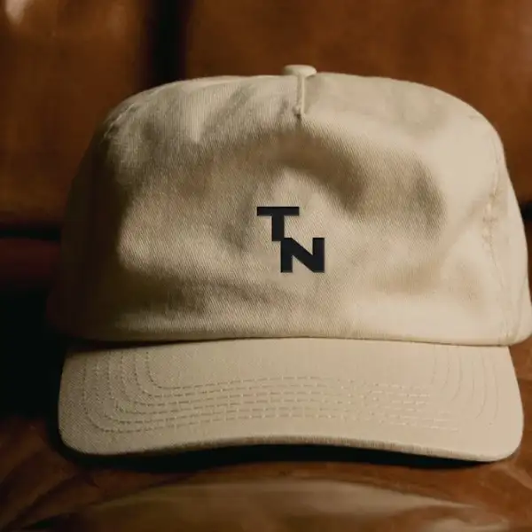 Gorra beige de Tinto con el logo TN bordado en negro al frente, apoyada sobre un sillón de cuero